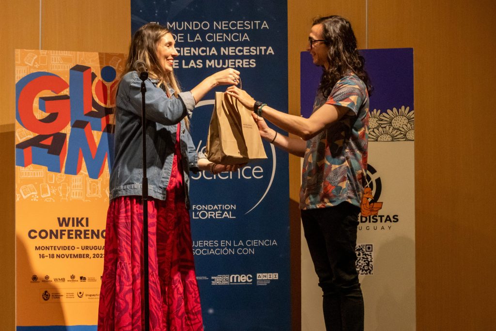 A woman stands at the stage with a package in her hands and delivers it to a man